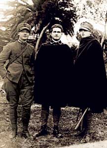 Tre militari dell'Arma a piedi in uniforme di panno grigio-verde da esercitazione. Quello al centro porta i gradi da vice brigadiere sul collo della mantellina.